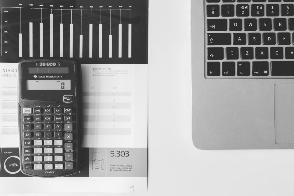 A calculator on printed charts next to a laptop keyboard, the tools for working out a discount from the right reference price