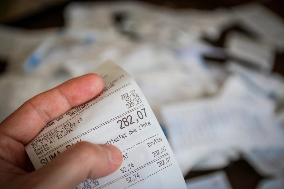 Une main tient un long ticket de caisse, le moment où le client voit tous les frais facturés