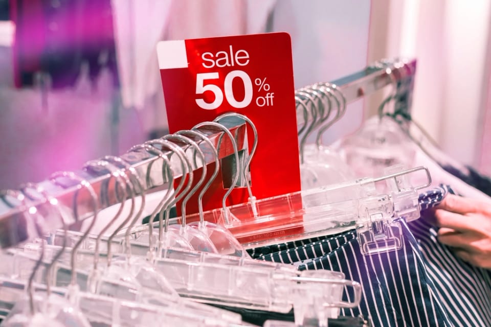 Une pancarte rouge « sale 50 % off » au-dessus d'un portant de vêtements, une réduction soumise à la règle des 30 jours