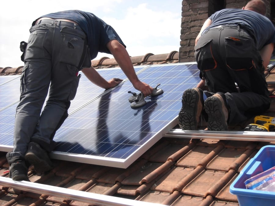 Zwei Monteure installieren Solarmodule auf einem Ziegeldach, eine echte Reduktionsmaßnahme statt einer gekauften Kompensation