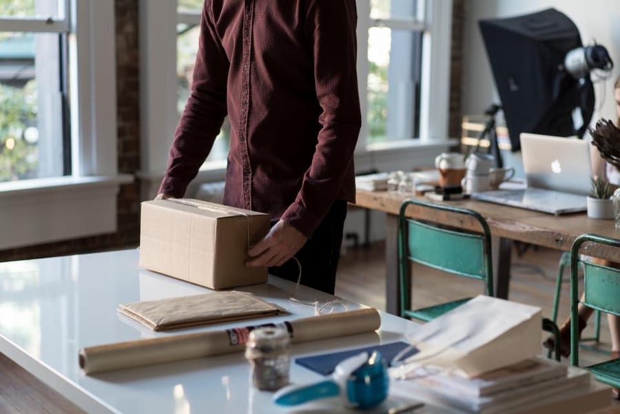 Eine Person packt an einem Schreibtisch mit aufgeklapptem Laptop eine Online-Bestellung, das Online-Geschäft, für das keine Erleichterung gilt