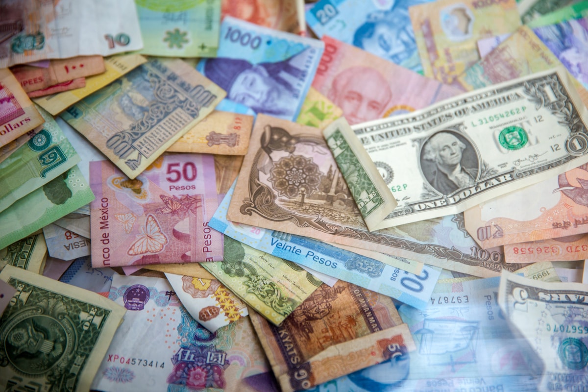 Billets de plusieurs monnaies — euro, dollar, peso, roupie — superposés sur fond sombre, illustrant l'empilement des sanctions entre juridictions sous coordination CPC