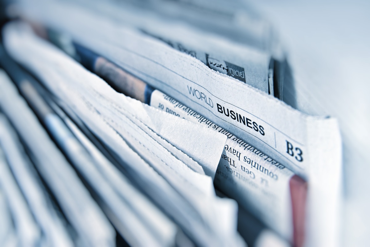 Journaux pliés de la rubrique économique empilés, le titre 'WORLD BUSINESS' visible dans le cadre — la cadence médiatique derrière chaque amende UE pour greenwashing
