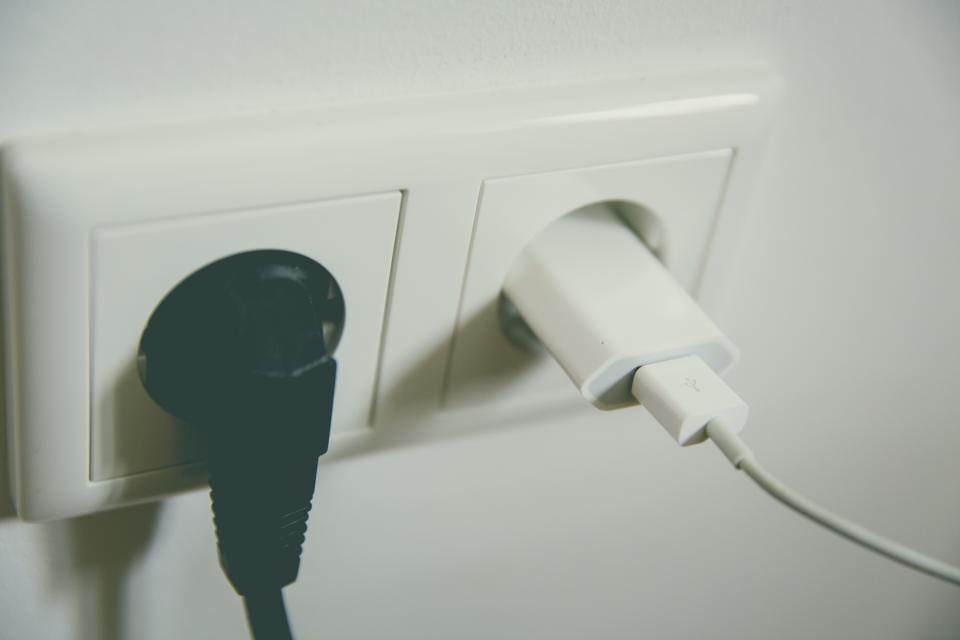Un caricatore bianco inserito in una presa a muro accanto a una spina nera, apparecchi elettrici le cui istruzioni di sicurezza vanno nell'offerta