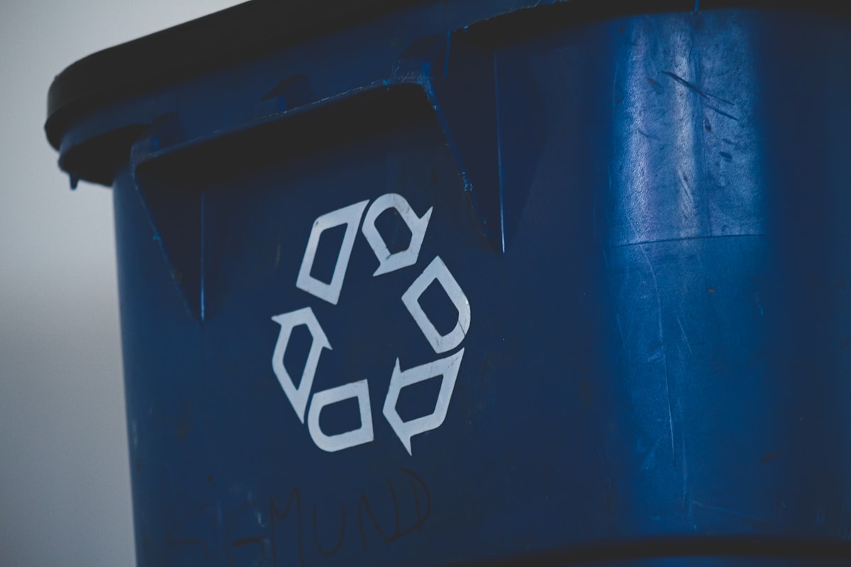 Gros plan sur le symbole de recyclage « flèches en boucle » (ruban de Möbius) sur un bac plastique bleu : la marque la plus détournée du greenwashing des emballages
