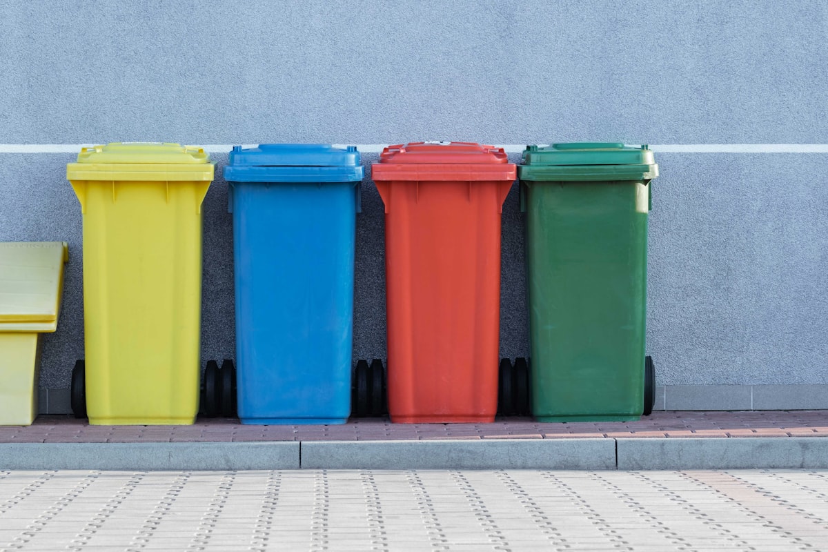 Rangée de quatre bacs de recyclage domestiques codés par couleur — jaune, bleu, rouge et vert — contre un mur gris