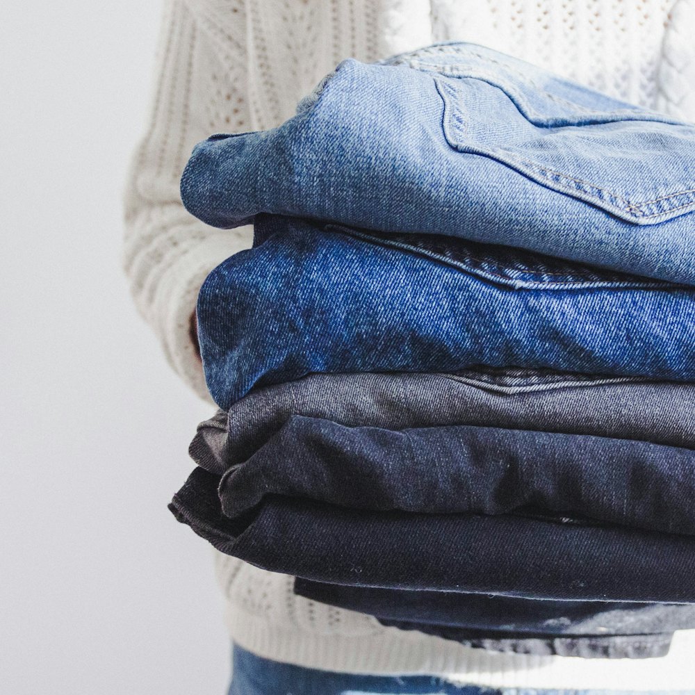 Stack of folded denim jeans held against a knit sweater — fast-fashion volume that compounds greenwashing exposure