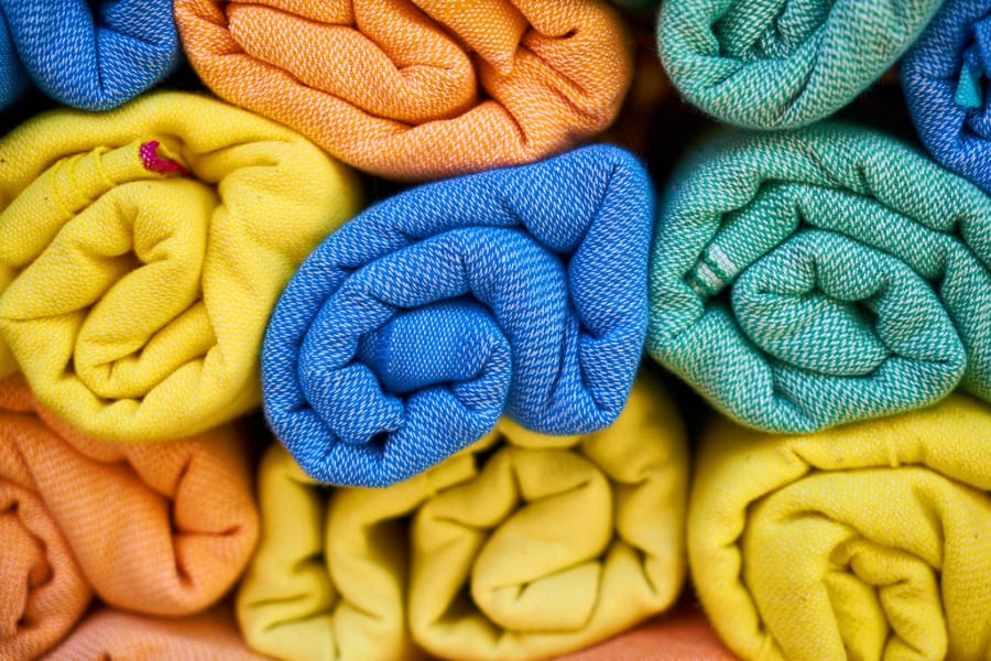 Aufgerollte Textilien in Blau, Gelb, Orange und Grün, übereinandergestapelt, die Art von Lieferantenmaterial, die mit Recycling- oder Bio-Aussagen ankommt